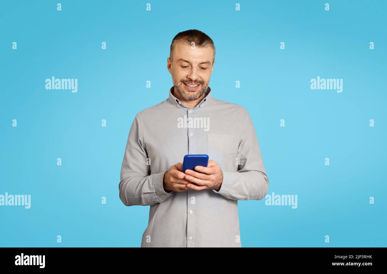 Mature Male Using Phone Texting And Websurfing Over Blue Background Stock Photo