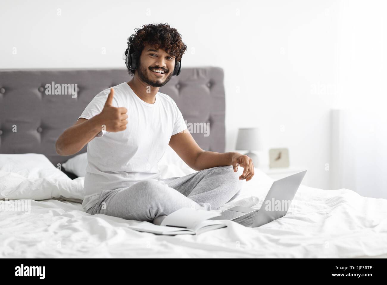 Positive eastern guy attending webinar, bedroom interior Stock Photo