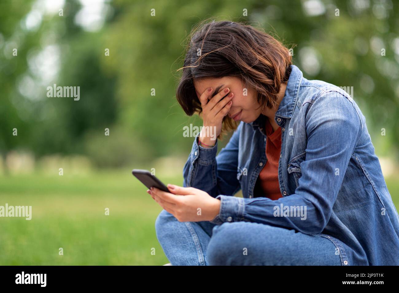 Depressed Young Arab Woman Sitting Outdoors With Smartphone In Hands And Crying Stock Photo