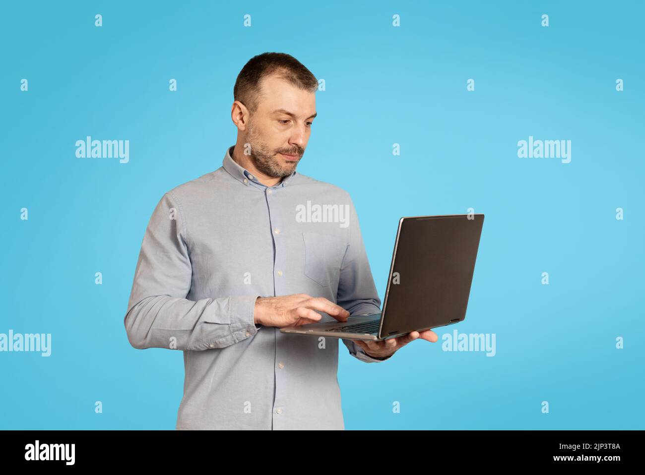 Middle Aged Businessman Using Laptop Computer Working Online, Blue Background Stock Photo