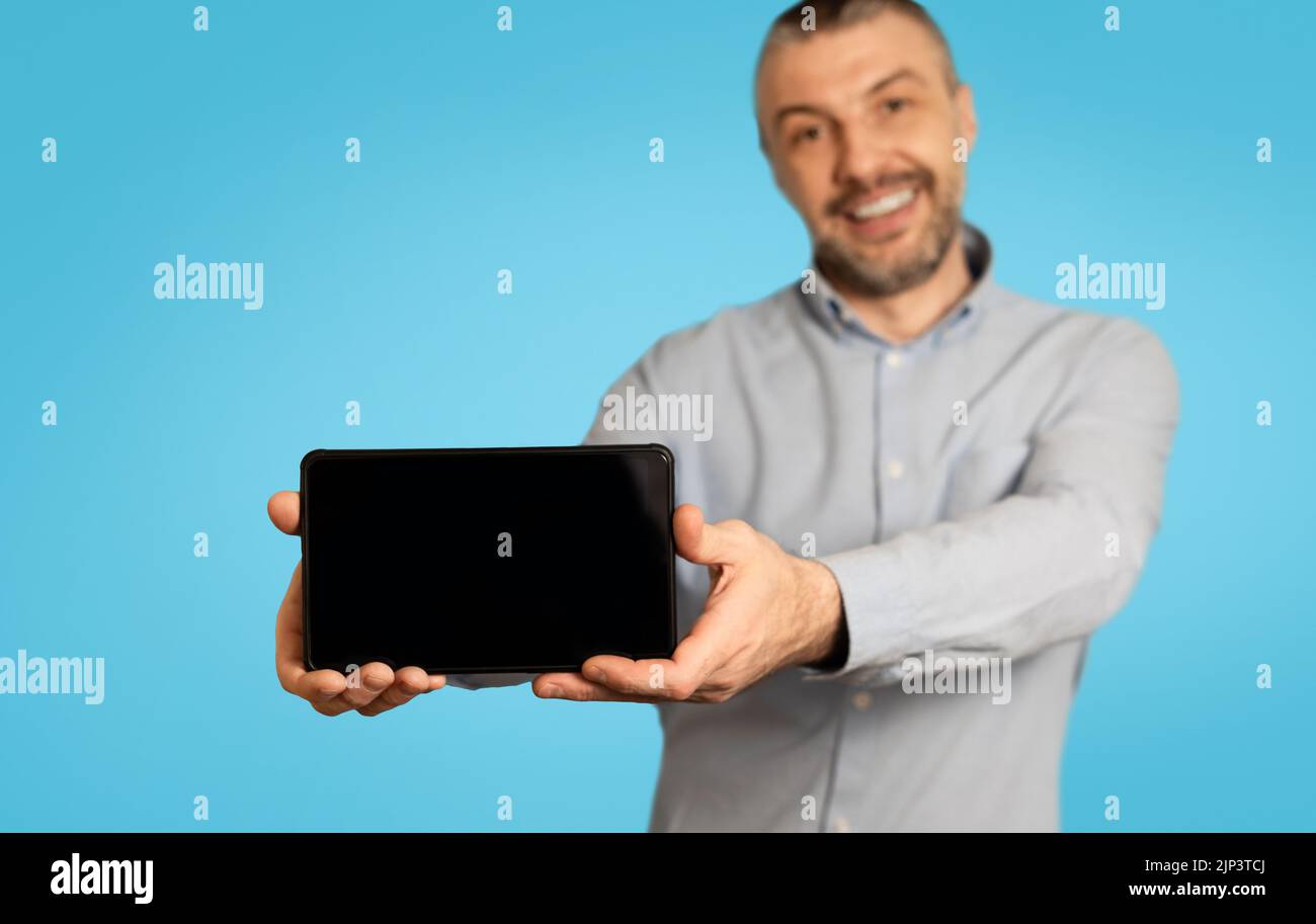 Cheerful Man Showing Mobile Phone With Blank Screen, Blue Background Stock Photo