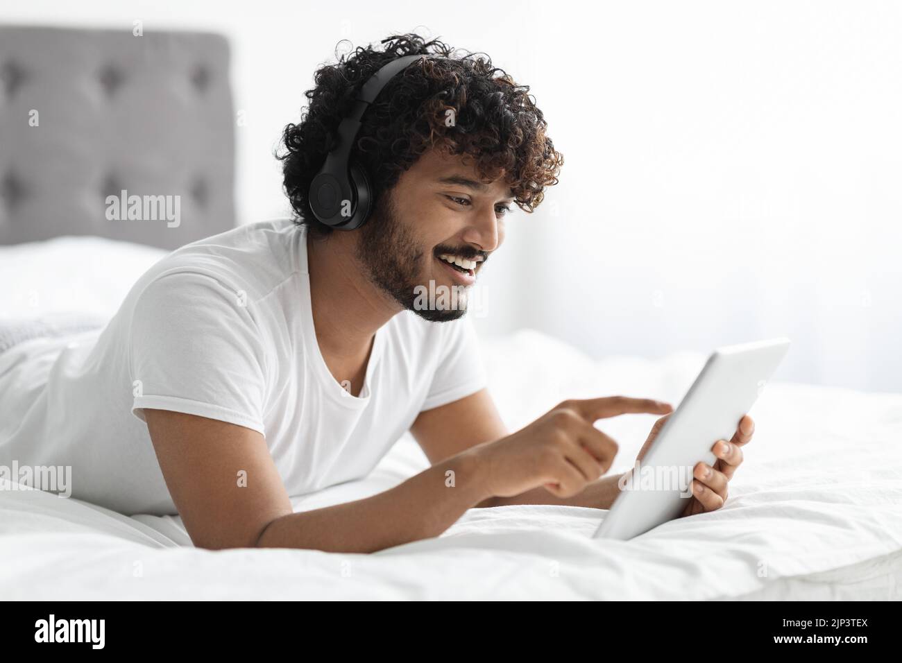 Relaxed hindu guy using digital tablet and headphones in bed Stock Photo
