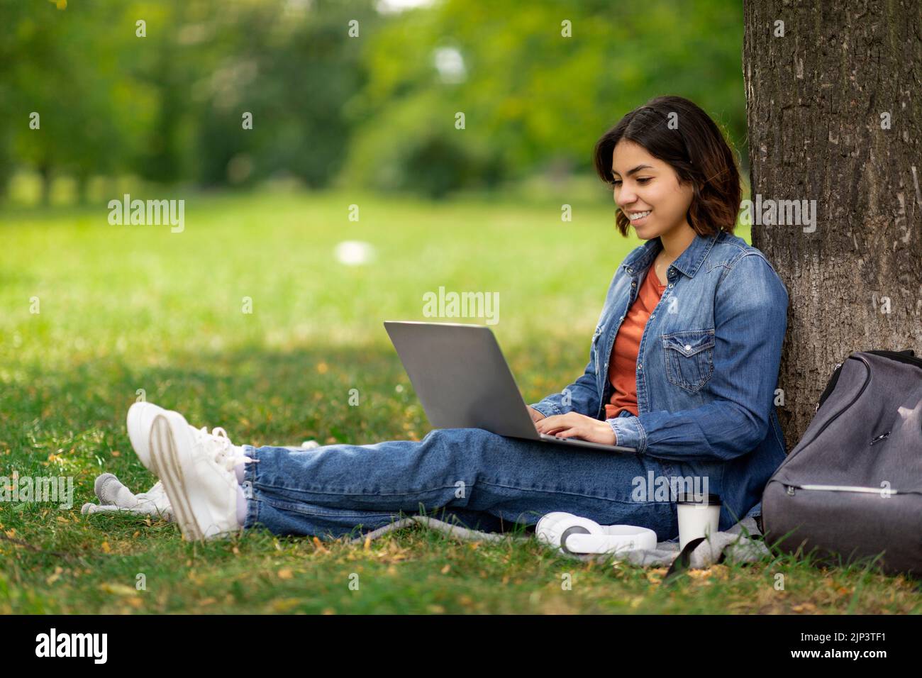 E-learning Concept. Arab Female Student With Laptop Sitting Under Tree In Park Stock Photo