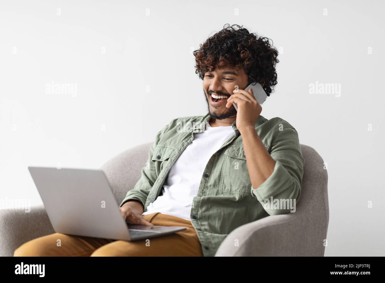 Positive handsome indian guy entrepreneur working online, having phone conversation Stock Photo