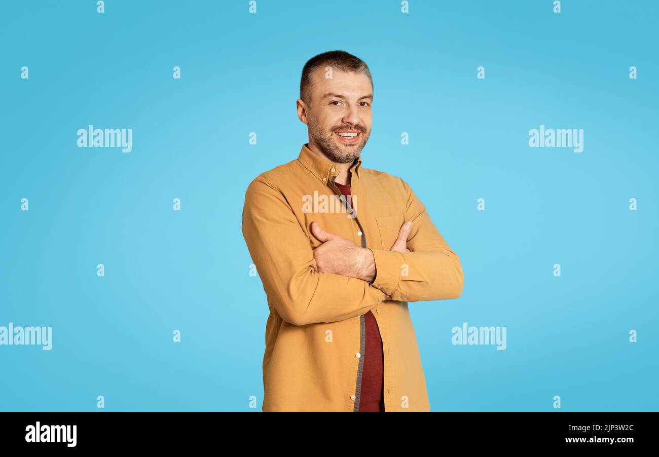 Mature Man Posing Crossing Hands Standing On Blue Studio Background Stock Photo