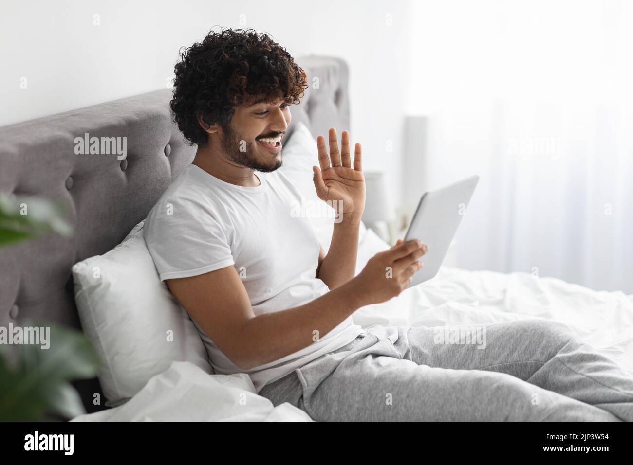 Happy indian guy sitting on bed, having video call Stock Photo