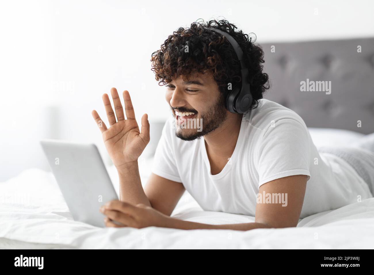 Handsome indian guy lying on bed, having video conference Stock Photo