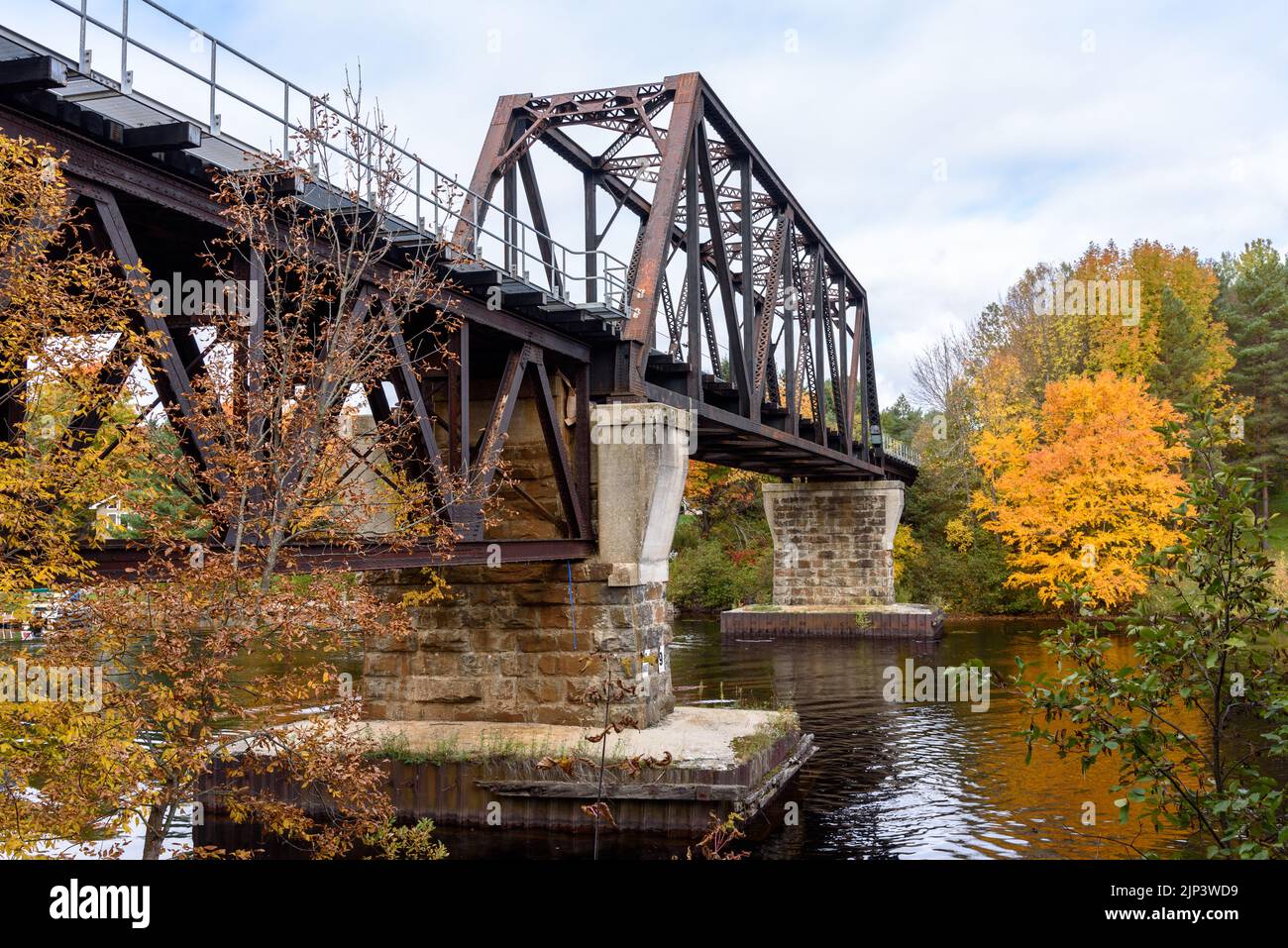 Old metal railroad bridge spanning a river on a cloudy autumn day Stock Photo