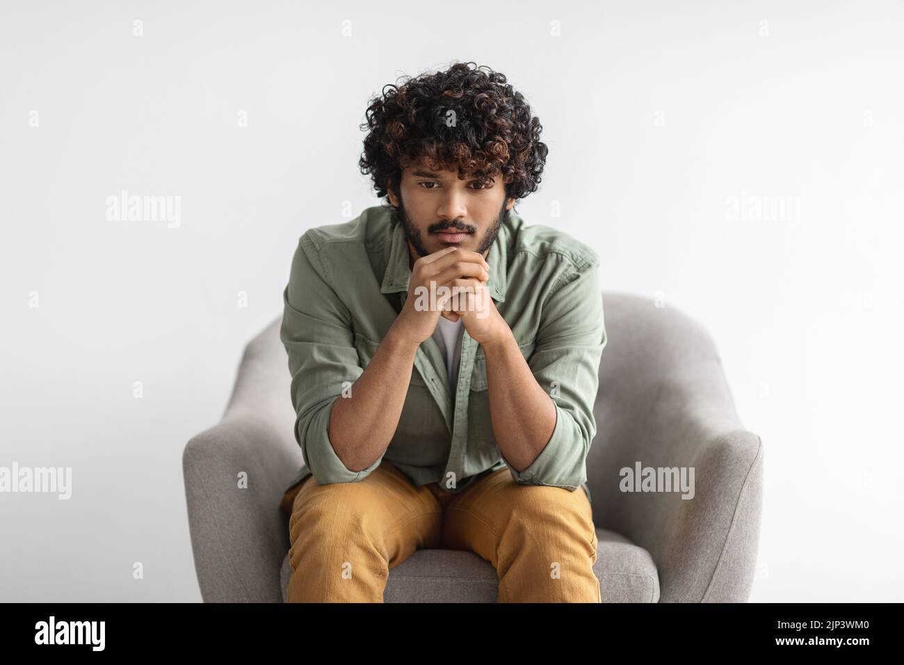 Pensive indian guy sitting in armchair over white Stock Photo