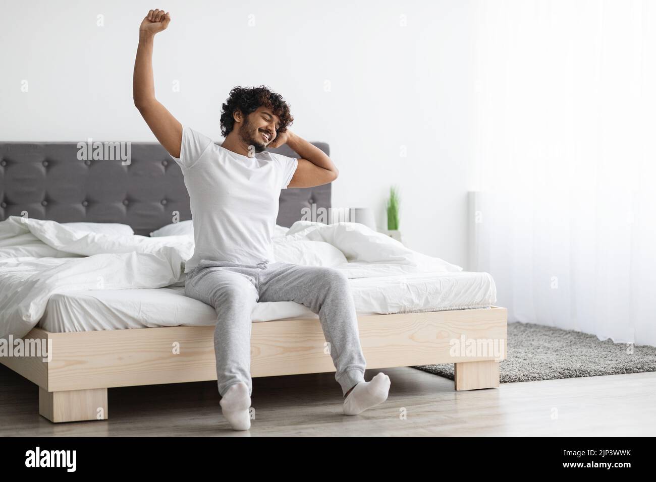 Cool eastern millennial guy stretching in bed Stock Photo