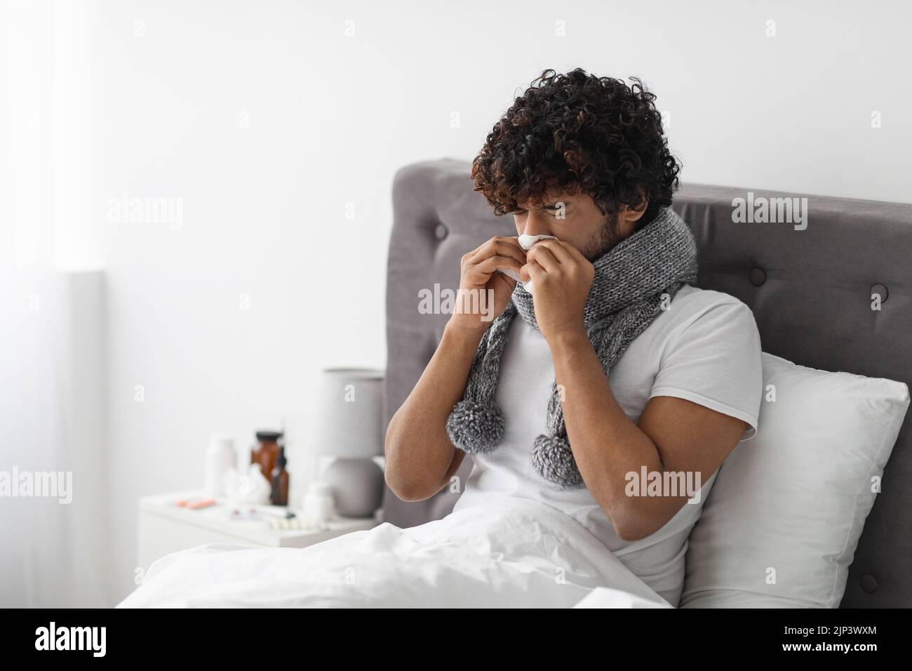 Sick eastern guy staying in bed, sneezing nose Stock Photo