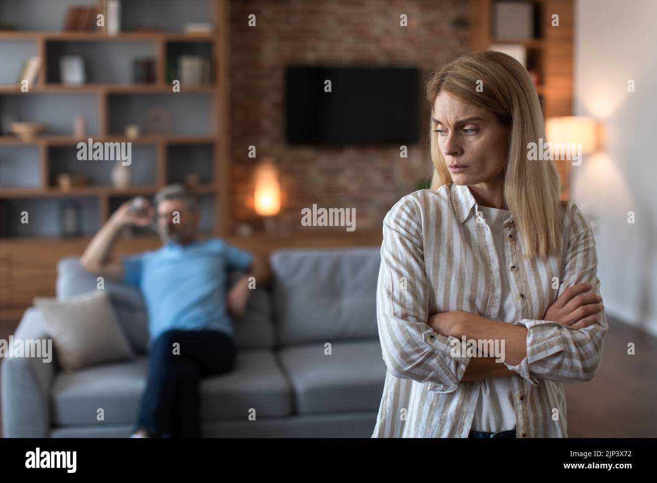 Upset offended middle aged caucasian wife ignores angry sad husband in living room interior. Conflict, stress Stock Photo