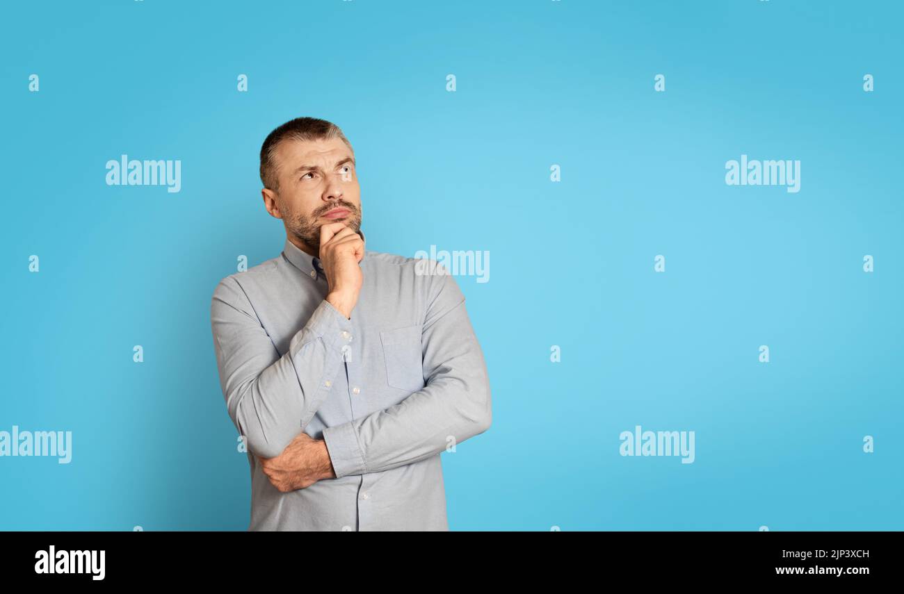 Thoughtful Middle Aged Man Thinking Touching Chin On Blue Background Stock Photo