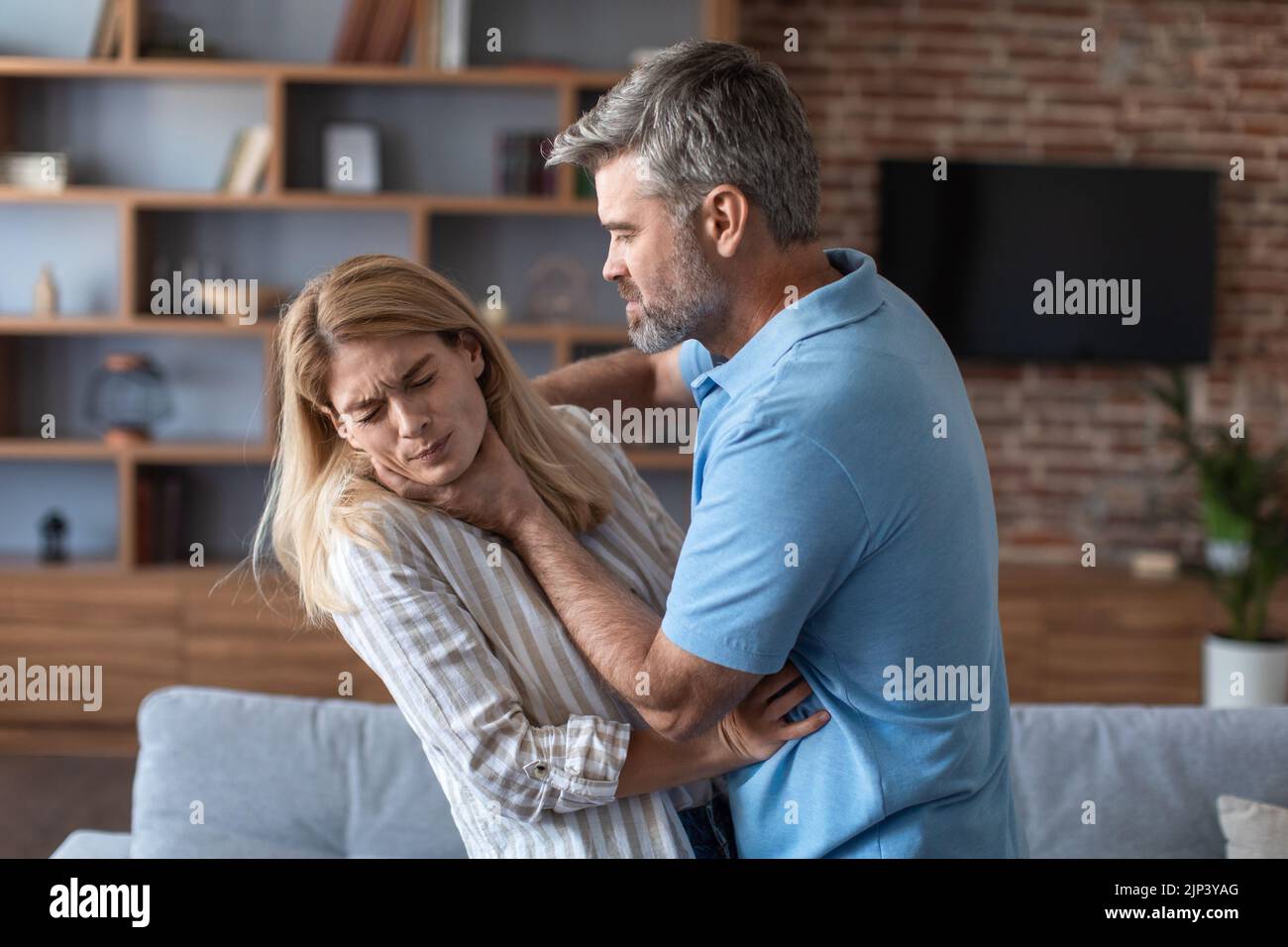 Aggressive angry european husband strangles behind proud frightened afraid wife in living room interior Stock Photo