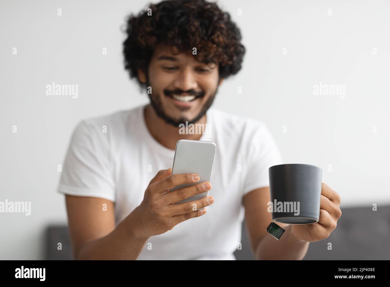 Smiling indian man drinking coffee and using smartphone Stock Photo