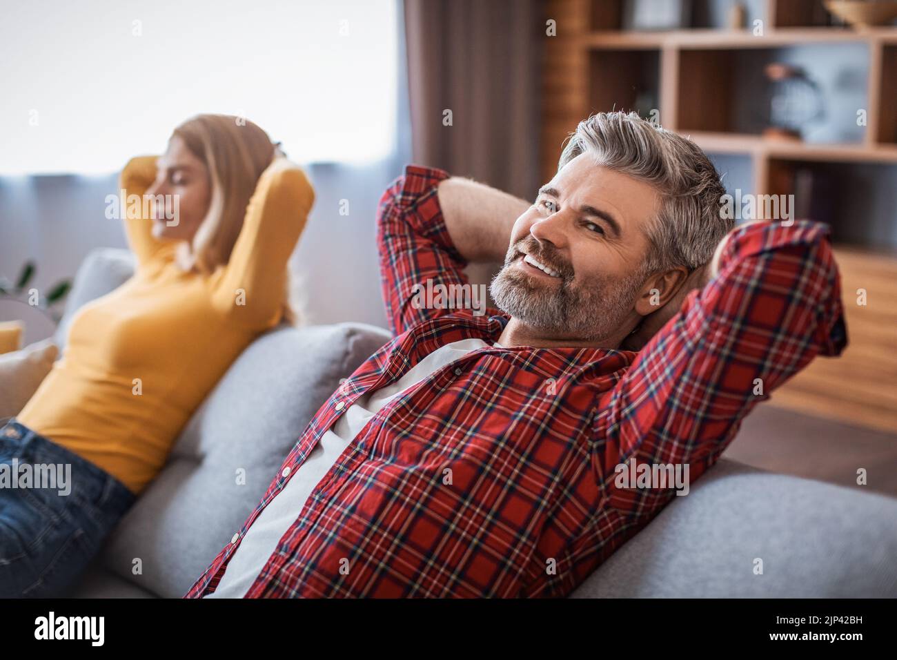 Cheerful middle aged handsome european man and woman enjoy rest and relaxation, dreaming on sofa Stock Photo