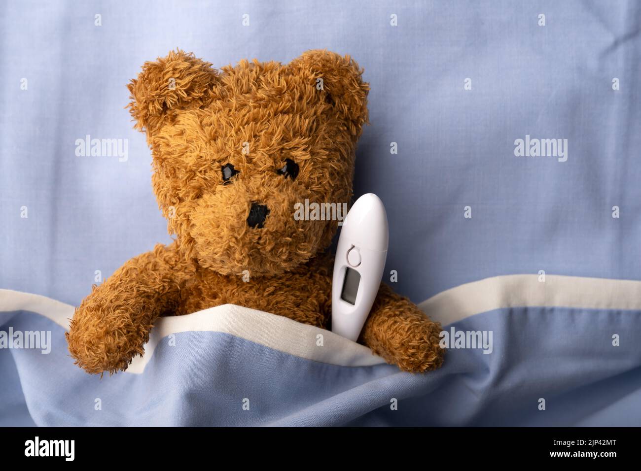 Sick teddy bear on hospital bed with thermometer. Pediatrical and child medicine concept Stock Photo
