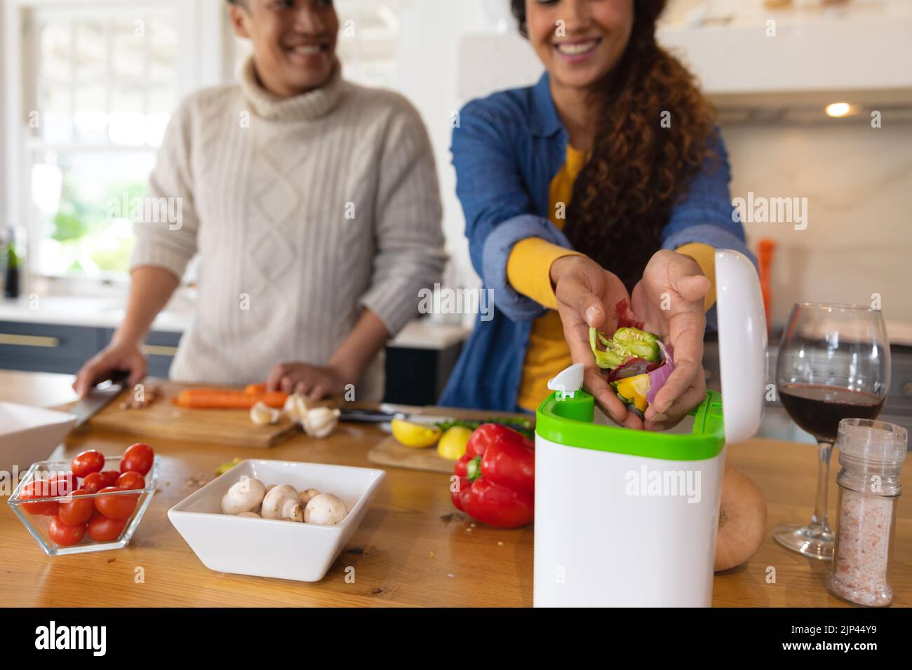 Happy biracial couple preparing food and composting vegetable waste in kitchen Stock Photo