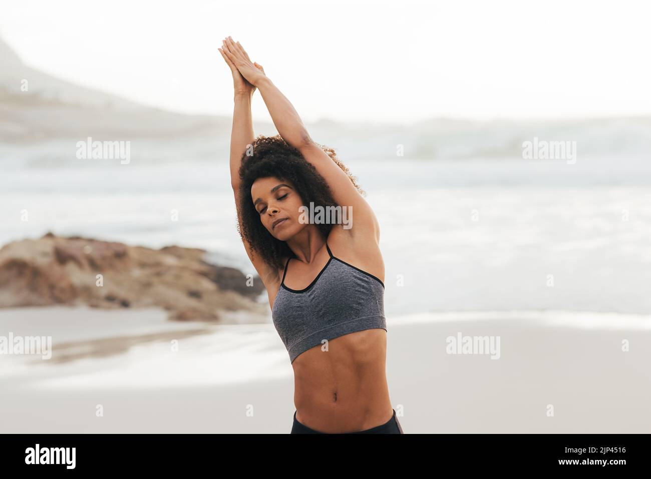 Fit woman standing on beach with eyes closed and stretching Stock Photo