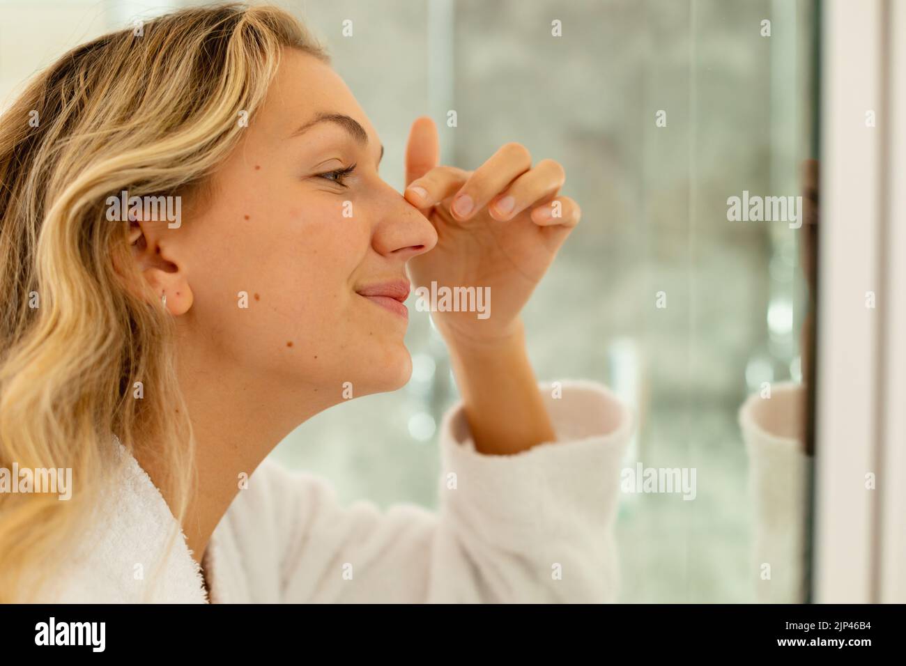 Happy caucasian woman wearing robe, looking at mirror and touching her ...