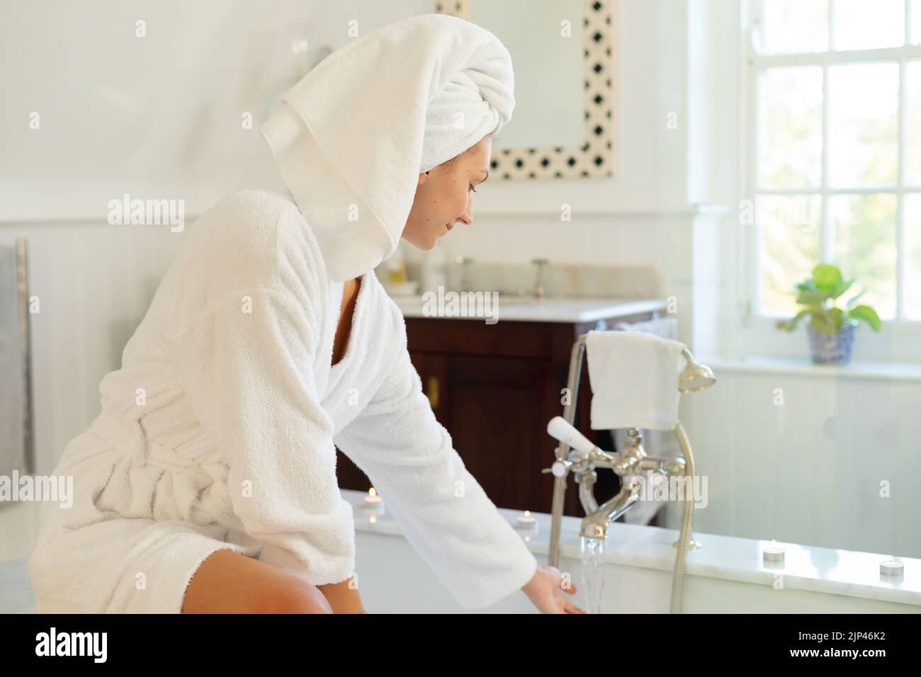 Happy caucasian woman wearing robe, running bath in bathroom Stock
