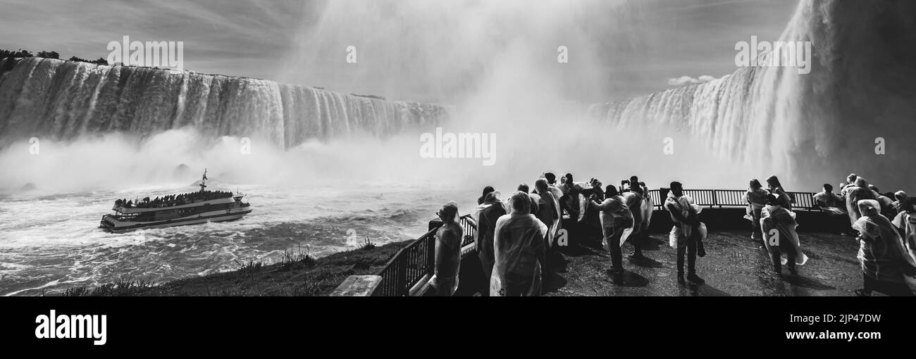 A panoramic grayscale of the beautiful Niagara Falls with tourists observing the cruise on the river Stock Photo