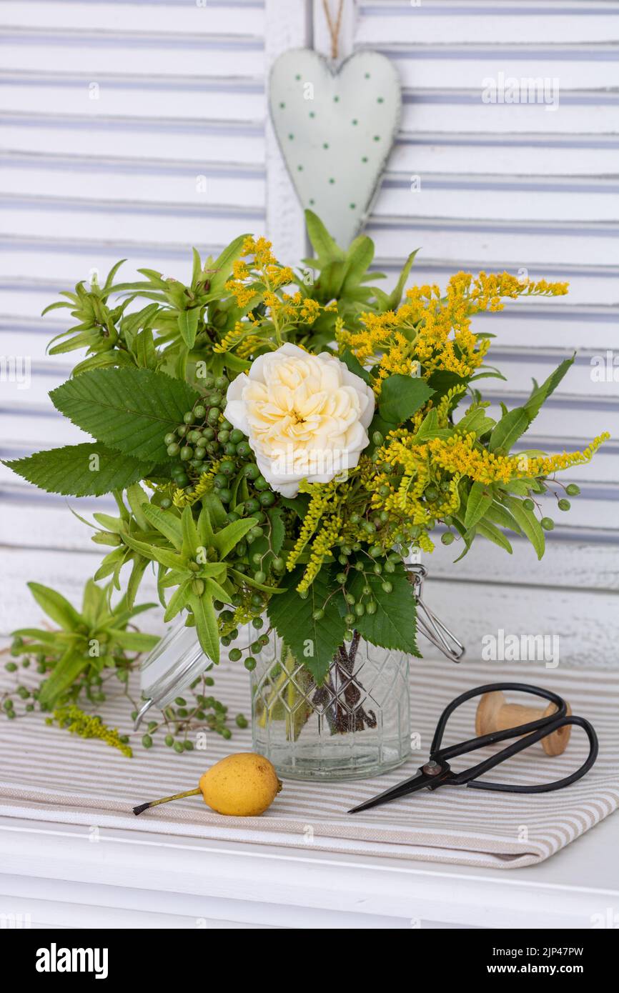 bouquet of white rose, hazelnut tree fruits, goldenrod and elder berries in glass Stock Photo
