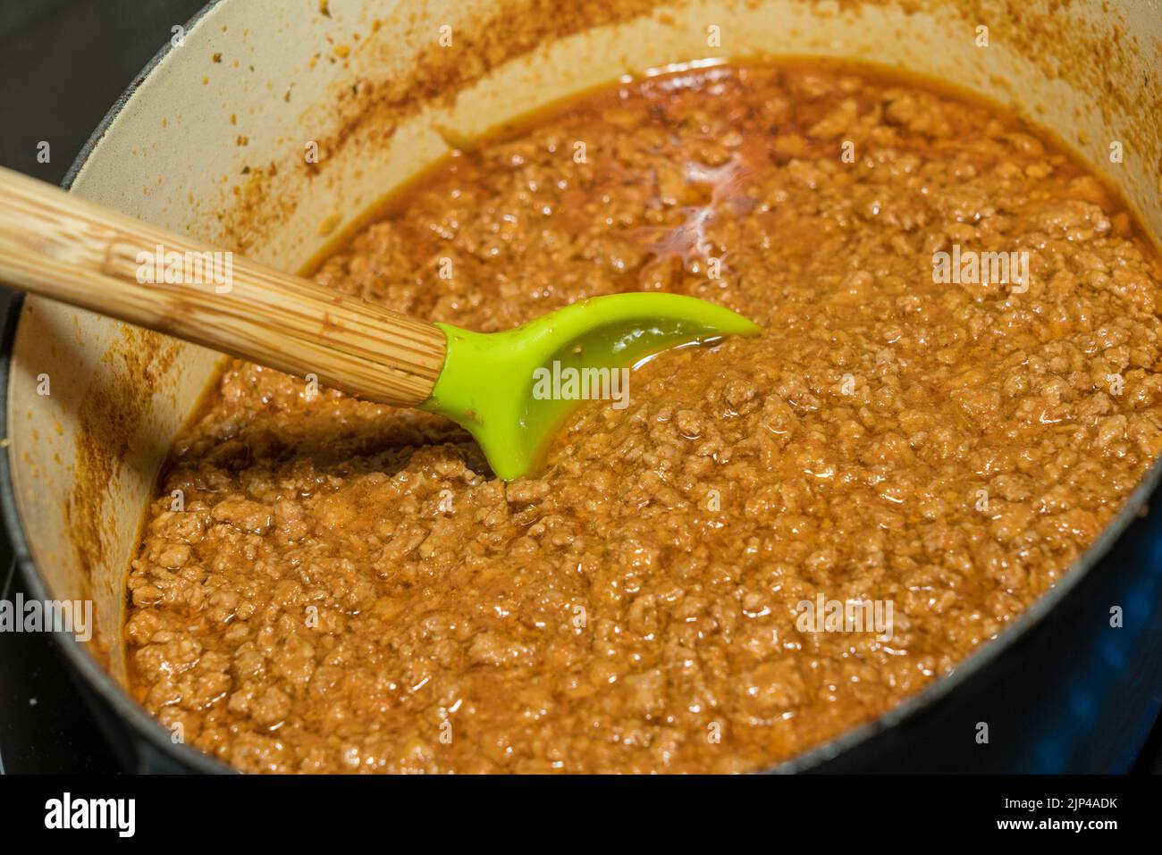 Spoon in simmering pot of home made ragu or ragout in cast iron pot on stove Stock Photo