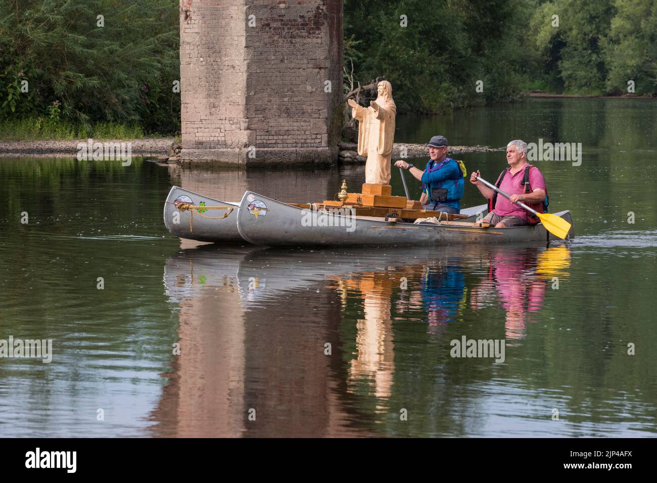 The Voyage of Our Lady of the Waters and the Wye. A newly carved wooden statue of the Virgin Mary is being floated 75 miles down the River Wye, from Hay-on-Wye to Monmouth, from the 15th - 19th August 2022. The sculptor, Philip Chatfield (in pink) and a friend, Callum Bulmer (in blue), are making the journey to raise awareness of the high levels of pollution in the Wye, one of Britain's most important and beautiful rivers. They are seen here passing under the old bridge at Bredwardine, Herefordshire. Stock Photo