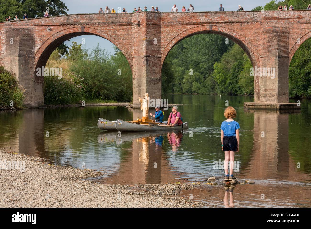 The Voyage of Our Lady of the Waters and the Wye. A newly carved wooden statue of the Virgin Mary is being floated 75 miles down the River Wye, from Hay-on-Wye to Monmouth, from the 15th - 19th August 2022. The sculptor, Philip Chatfield (in pink) and a friend, Callum Bulmer (in blue), are making the journey to raise awareness of the high levels of pollution in the Wye, one of Britain's most important and beautiful rivers. They are seen here passing under the old bridge at Bredwardine, Herefordshire. Stock Photo