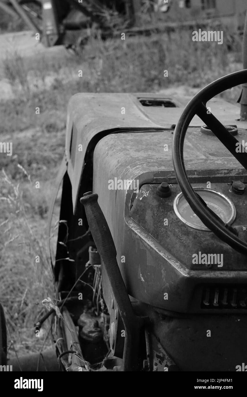 A vertical black and white shot of an old abandoned tractor on a field in a rural area Stock
