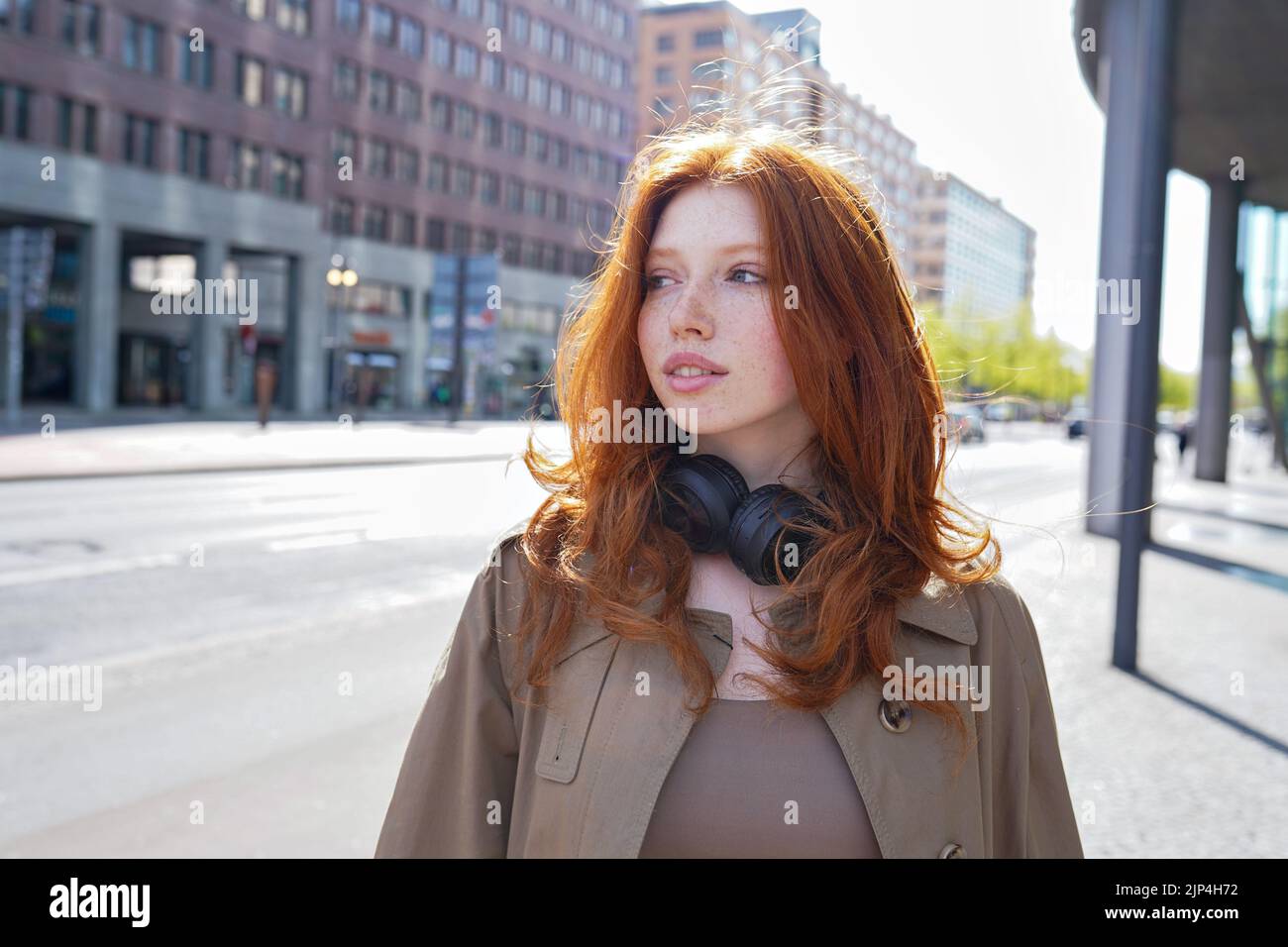 Teen hipster redhead girl looking at camera standing on urban street. Stock Photo