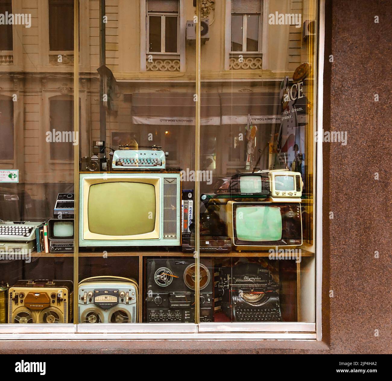 A collection of vintage TVs, radios, typewriters and other devices behind the window of an antique shop in Bucharest, Romania Stock Photo