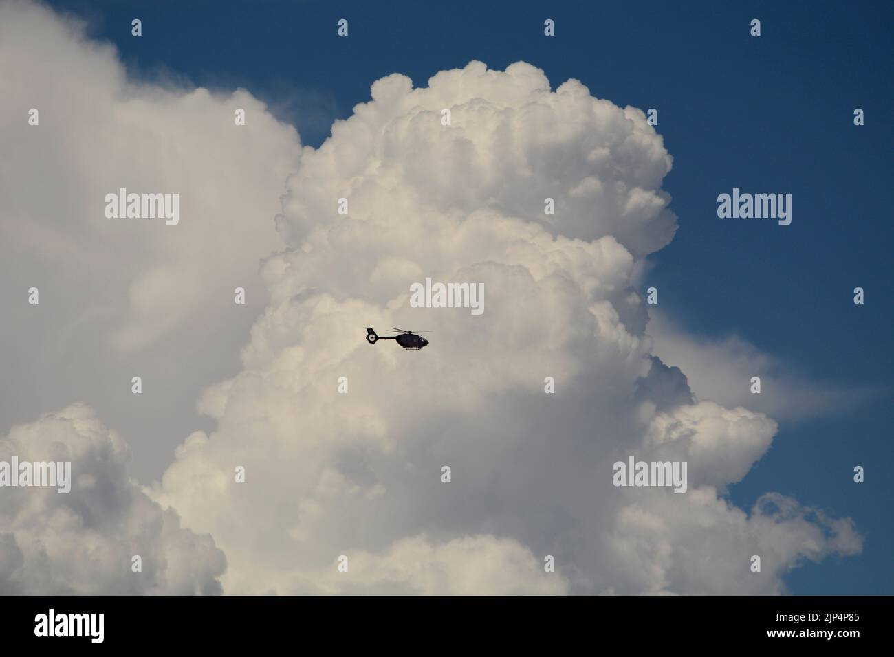 An Airbus Deutschland MBB-BK helicopter flies in front of towering cumulus clouds over Santa Fe, New Mexico. Stock Photo