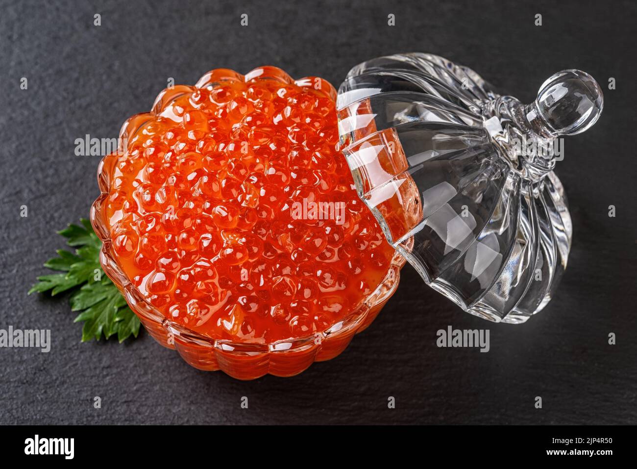 Salmon caviar in a crystal bowl with lid over black background. Glass dish full of chum red caviar closeup. Salted salmon roe for gourmet food concept Stock Photo