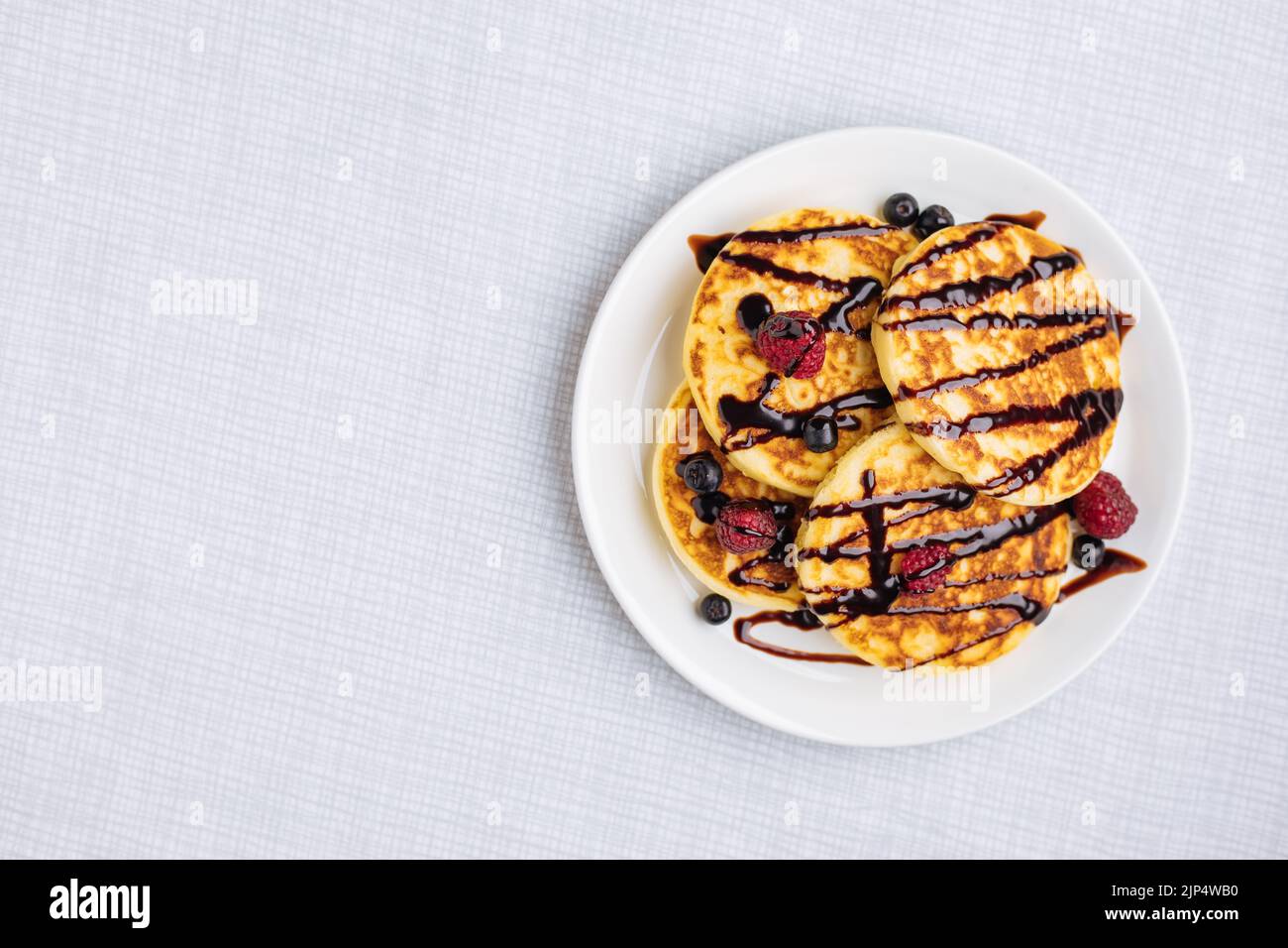 American pancakes decorated like smile and happy faces with raspberries, blueberries and banana. Food for kids, playful and creative. Top view. Stock Photo