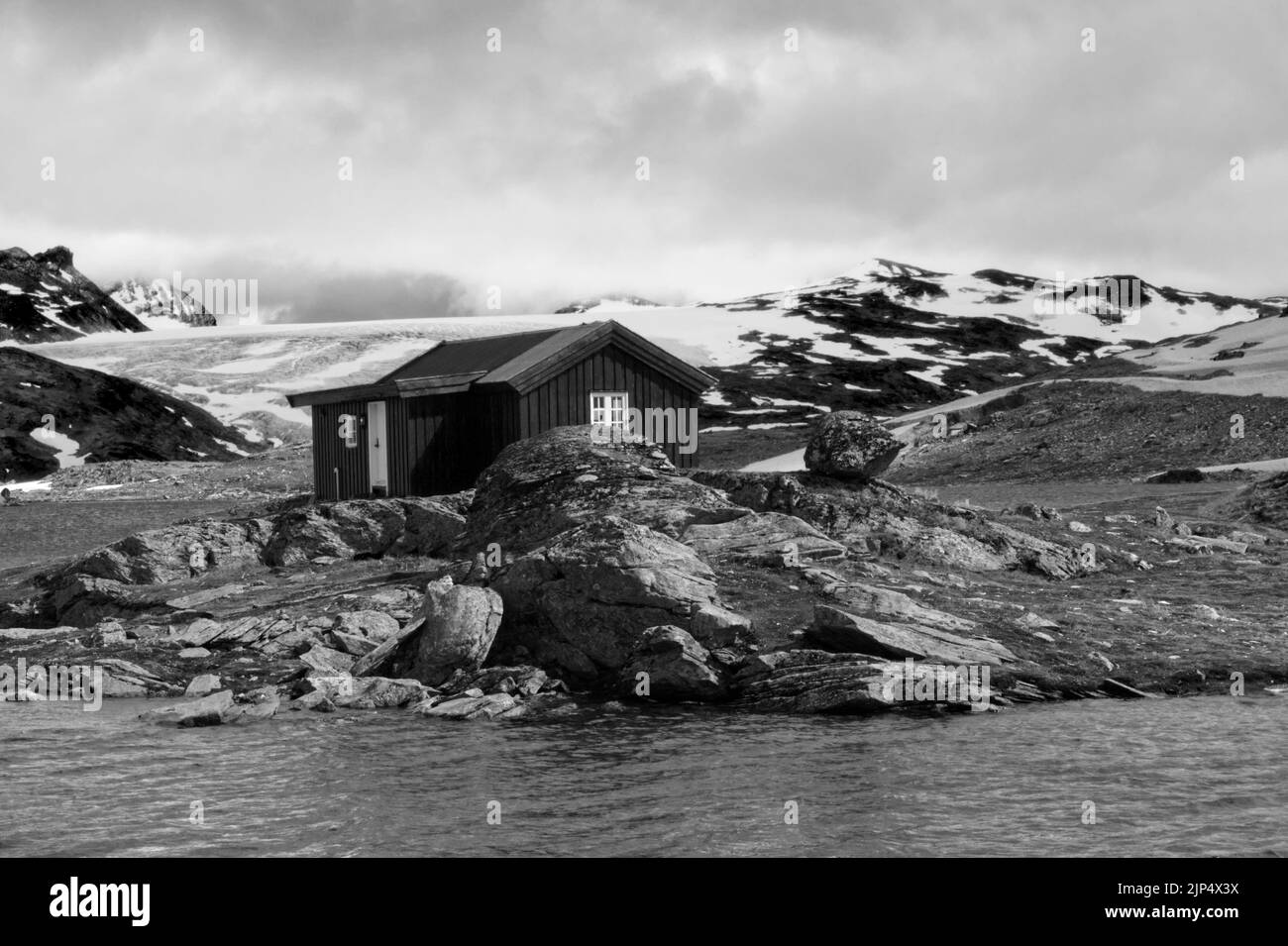 Norwegian black wooden house in the Nordic landscape by a glacial lake in black and white Stock Photo