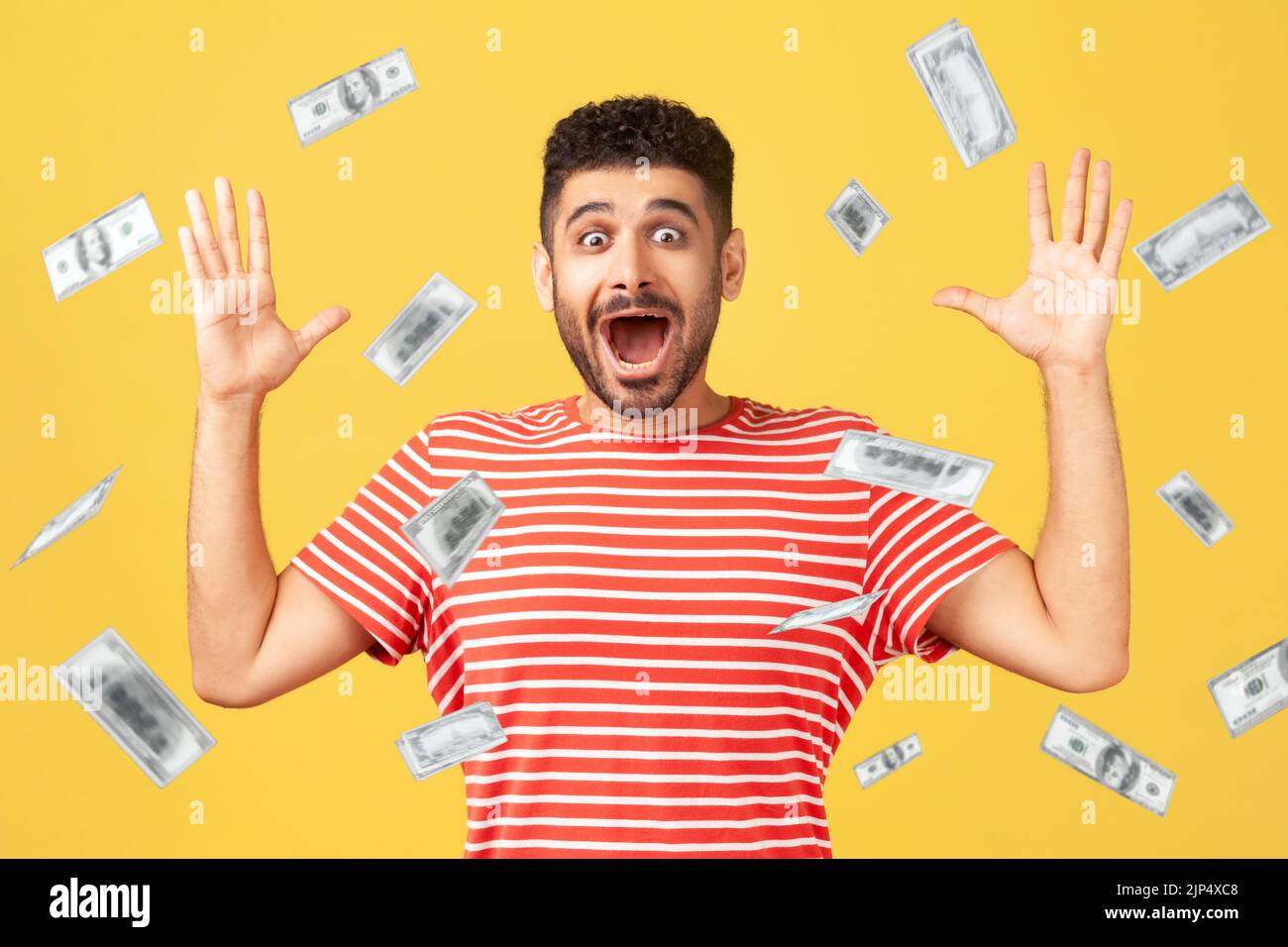 Oh my god, wow. Portrait of amazed man looking at camera with big eyes and open mouth, absolutely shocked of money rain falling from up. indoor isolated on yellow background Stock Photo