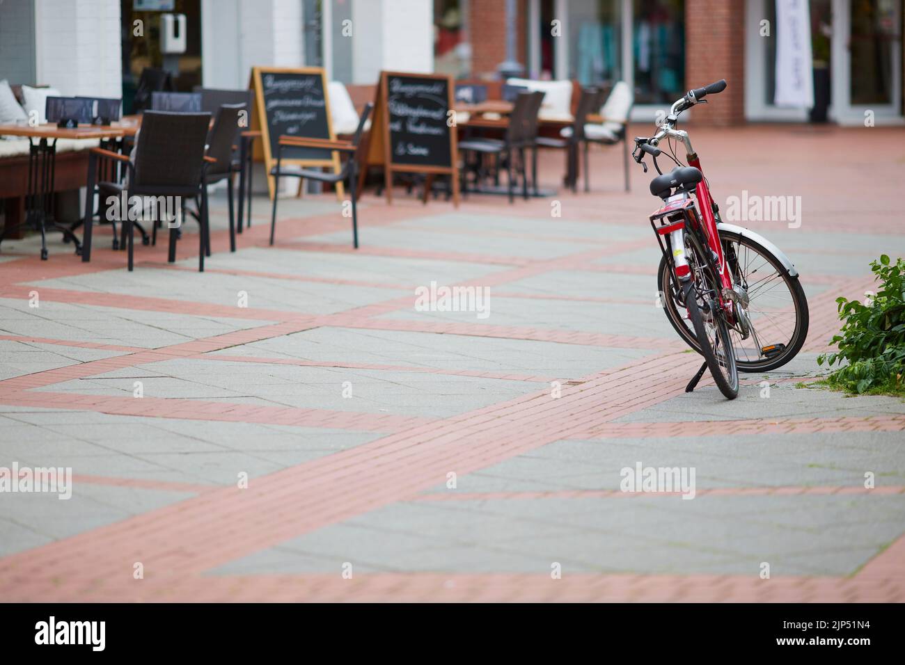 A red bicycle parked in the city next to a cafe outdoor seating Stock Photo