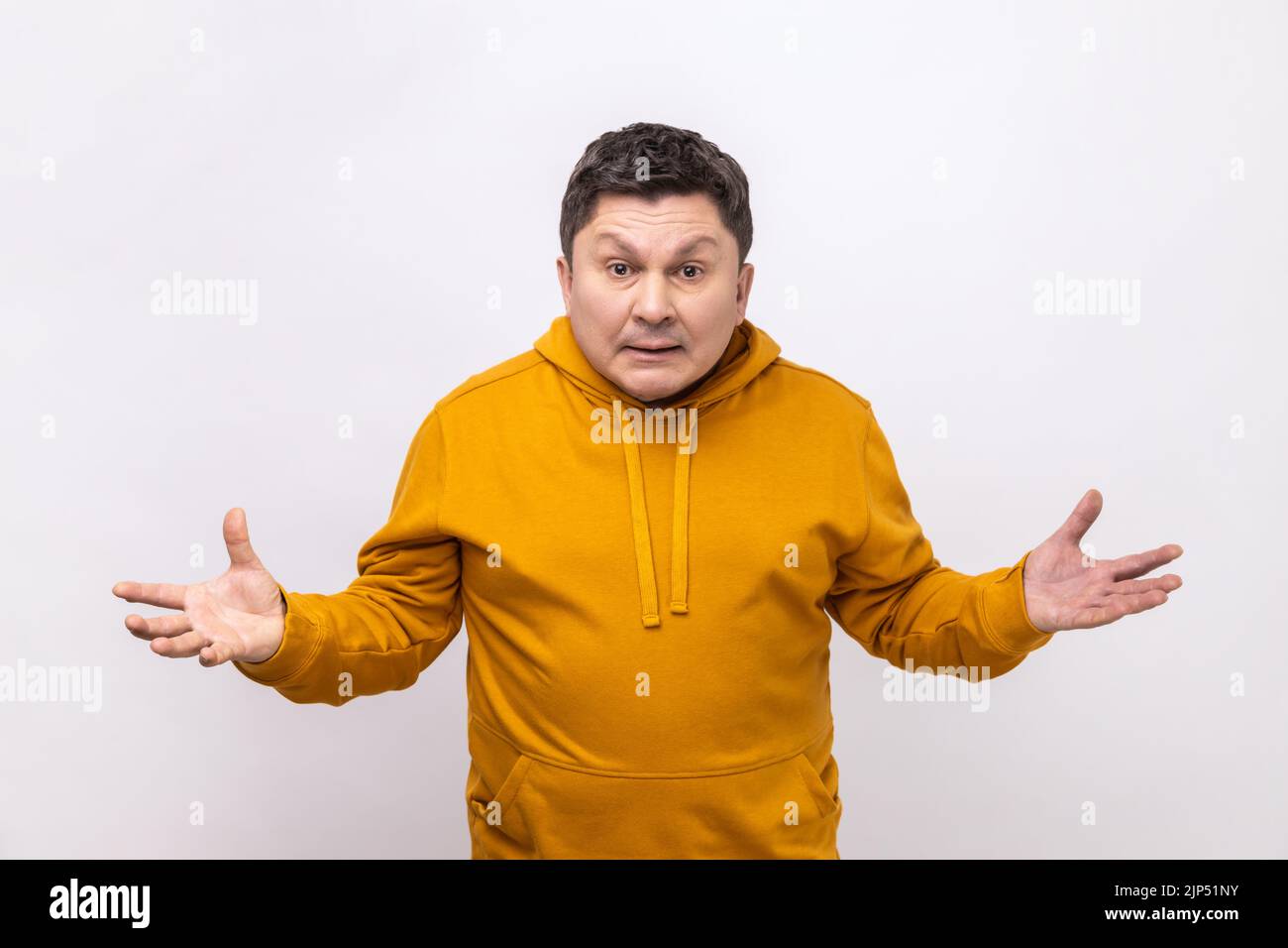 Portrait of angry confused man standing with raised hands and surprised indignant expression, asking why how, what reason, wearing urban style hoodie. Indoor studio shot isolated on white background. Stock Photo