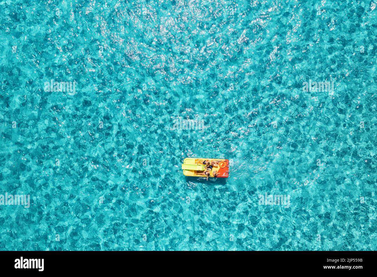 Relaxing people on the colorful boat in blue sea at sunny bright day. Summer vacation in Sardinia, Italy. Top view from drone of catamaran in transpar Stock Photo
