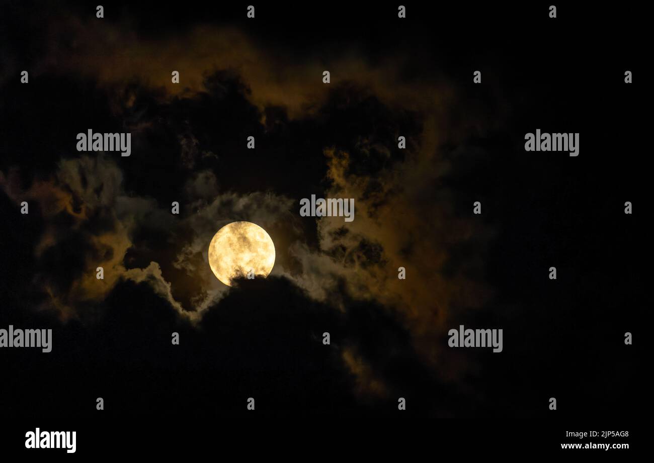 Full moon glow illuminates clouds on dark night Stock Photo