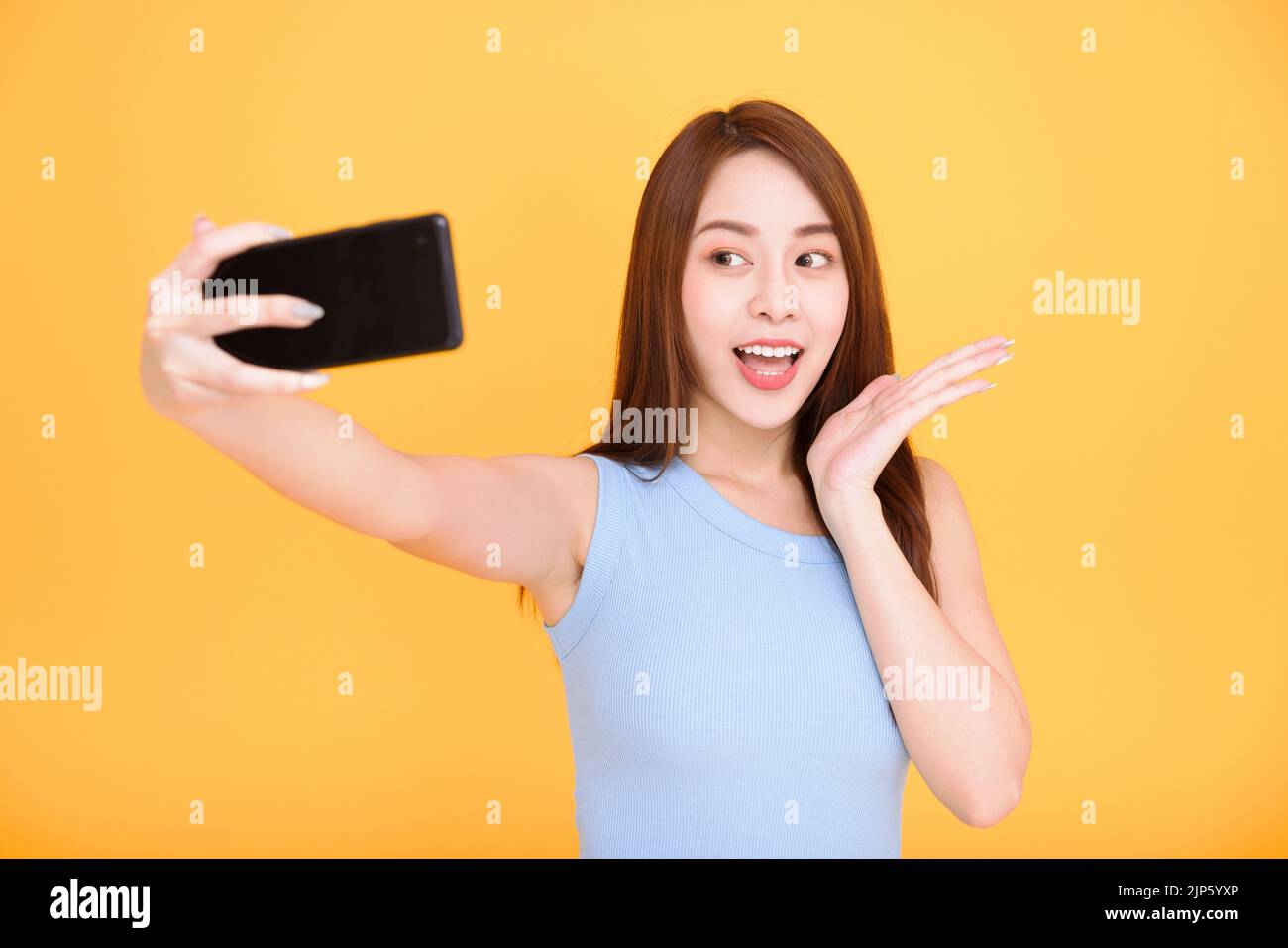 Young woman smiling and taking selfie photo on cellphone isolated over yellow background Stock Photo