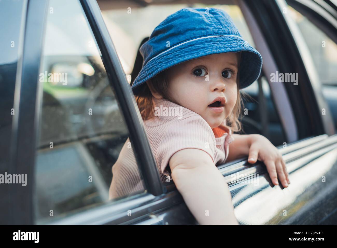 Baby girl sticking his head out of a car window, looking back to the camera. Cars heading forward to travel to natural places. Stock Photo