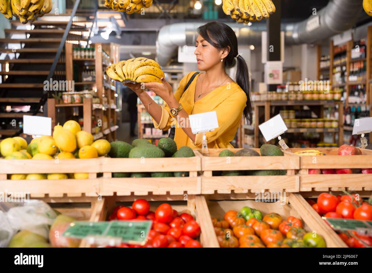 Woman choosing bananas in fruit and vegetable section of supermarket