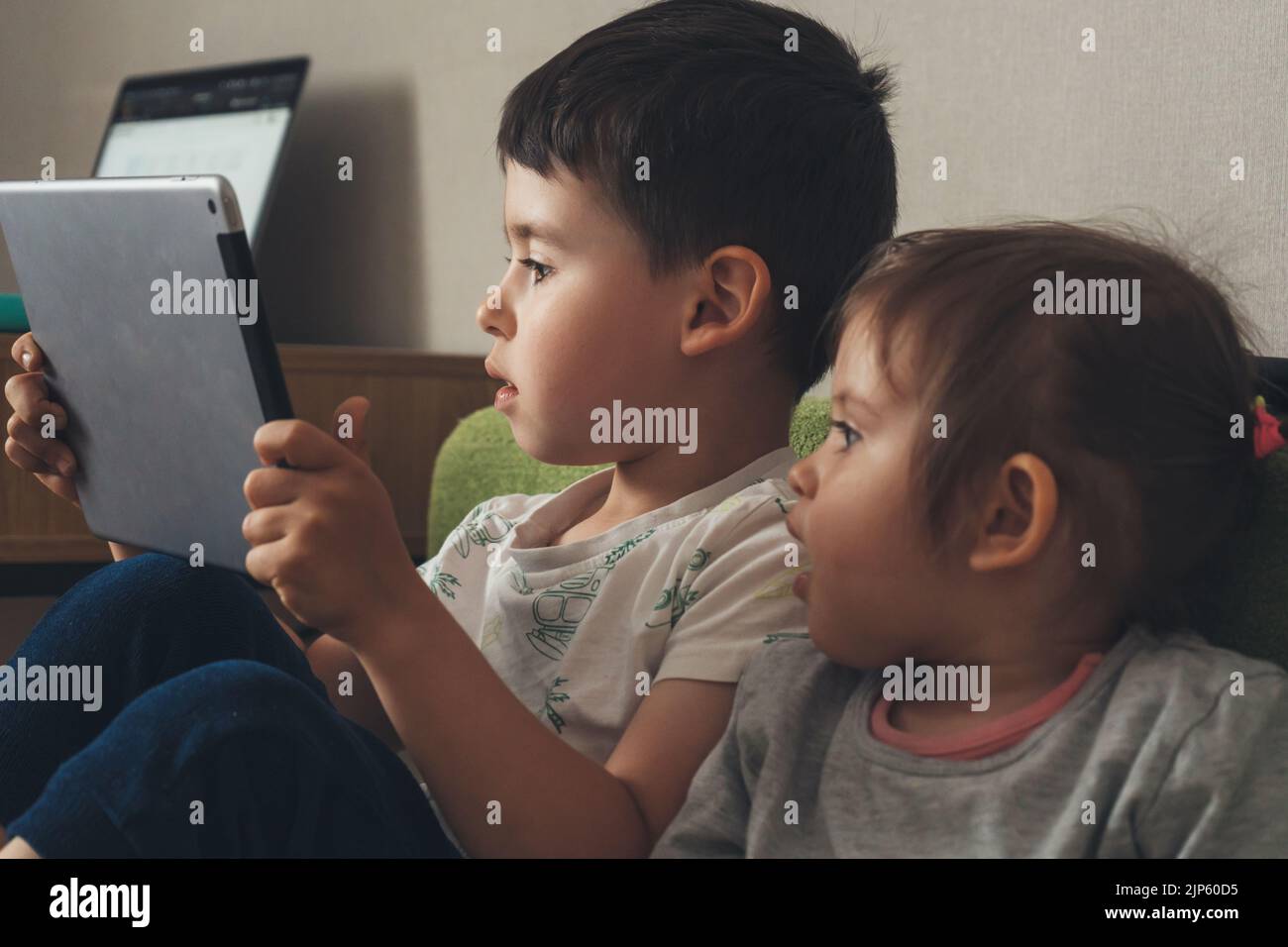 Two little kids playing games on a computer tablet together, sitting on