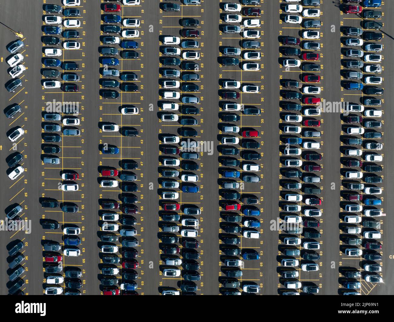 A direct overhead aerial view above a parking lot of newly manufactured cars, outside of a manufacturing plant. Stock Photo