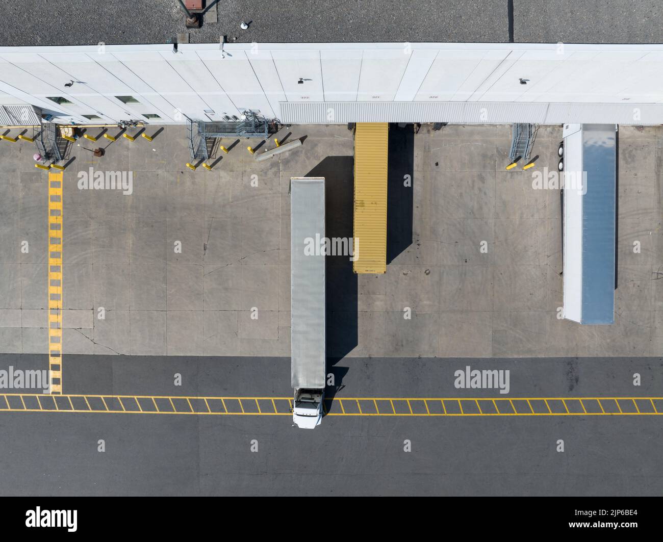 A direct top-down aerial view above a semi-truck, tractor trailer being parked at a large warehouse; other trailers are seen at loading docks. Stock Photo