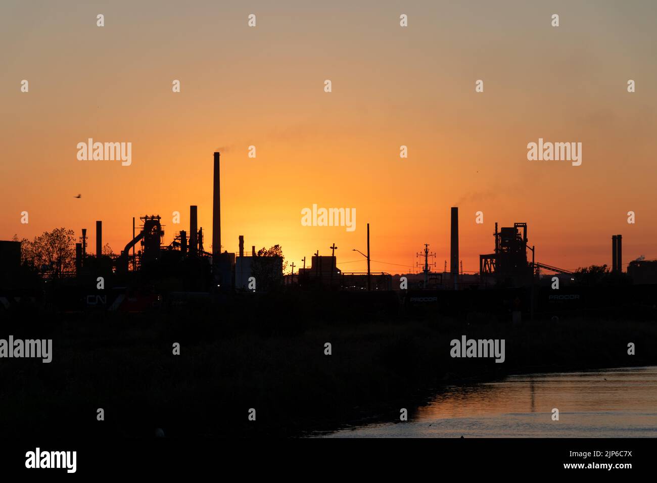 An industrial landscape in the Port of Hamilton is seen at dusk, smokestacks and factories are seen dark along the waterfront horizon. Stock Photo