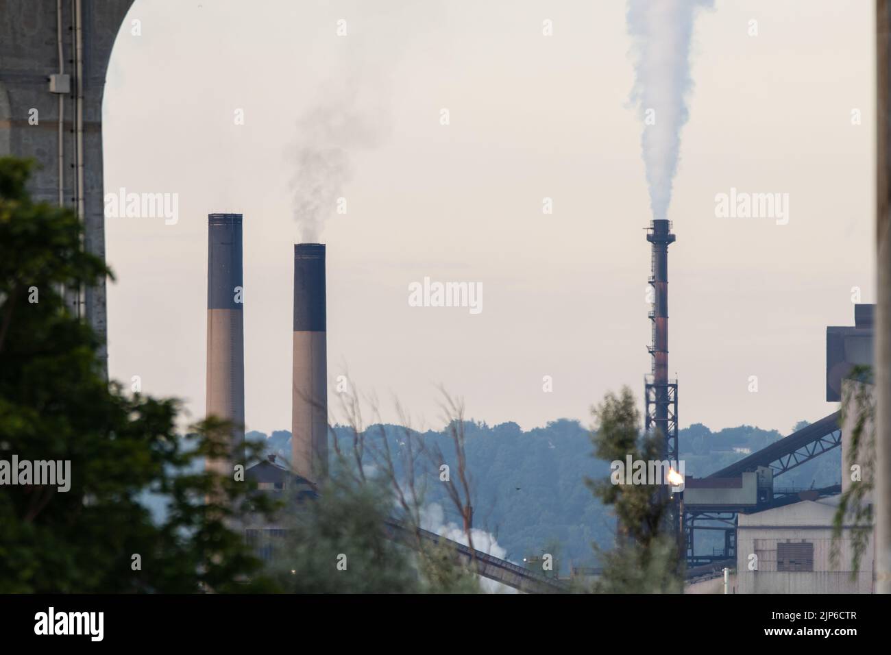 Smokestacks and a chimney at a large factory in a manufacturing sector area are seen as smoke, steam, and greenhouse gases travel into the air. Stock Photo